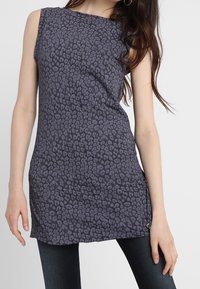 Sleeveless tunic in dark gray with a leopard print pattern. Made of soft fabric, featuring a straight cut and a side hem accent.