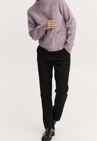 Světle fialová zipová mikina s ribbed texturou a vysokým límcem, spárovaná s černými elegantními kalhotami a lesklými černými mokasíny.