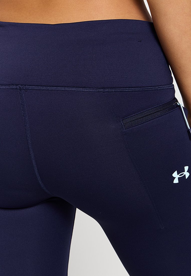 Leggings deportivos color azul marino con una textura suave, cintura alta y un pequeño bolsillo con cremallera en el lateral. Logotipo de Under Armour visible.