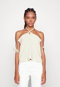Top halter de bege claro com recorte em forma de olho, mangas amarradas e silhueta fluida, combinado com calças brancas. Tecido suave e ajuste relaxado.