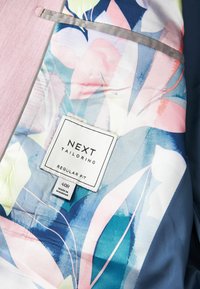 Skräddarsydd jacka med insida i färgglatt blommönster i blå, rosa och gröna nyanser. Etiketten säger "NEXT Tailoring, Regular Fit, 40R."