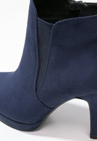 Námořnické modré semišové kotníkové boty s elegantním designem, s texturovaným povrchem, špičatou špičkou a 7,5 cm podpatkem, doplněné elastickými bočními panely.