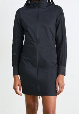 Czarna sukienka na zamek z gładkiego materiału, z wysokim kołnierzem, długimi rękawami i cienkimi pionowymi paskami na ramionach.