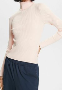 Suéter de cuello alto de color rosa claro con textura acanalada y mangas largas, de silueta ajustada. Combinado con pantalones de cintura elástica de color azul oscuro.