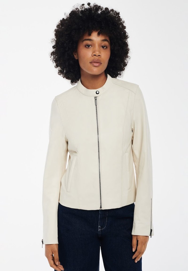 Giacca in pelle crema con colletto tondo, zip frontale e tasche laterali. Presenta cuciture strutturate e un design aderente.