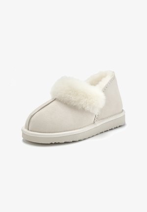 Beige Wildlederschuhe mit einem weichen weißen Fellkragen, abgerundeter Spitze und einer flachen Gummisohle; sichtbare Ziernähte entlang der Oberseite.