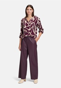 Blusa a maniche lunghe, scollo a V in viola con motivo astratto crema, abbinata a pantaloni a gamba larga prugna a vita alta e mule beige con tacco.