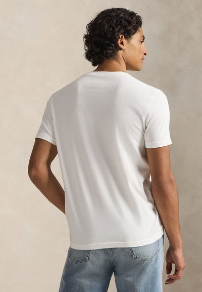 Λευκό βαμβακερό μπλουζάκι με κοντά μανίκια, στρογγυλή λαιμόκοψη και εφαρμοστή γραμμή, σε συνδυασμό με ανοιχτόχρωμο μπλε τζιν παντελόνι, θέα από πίσω.