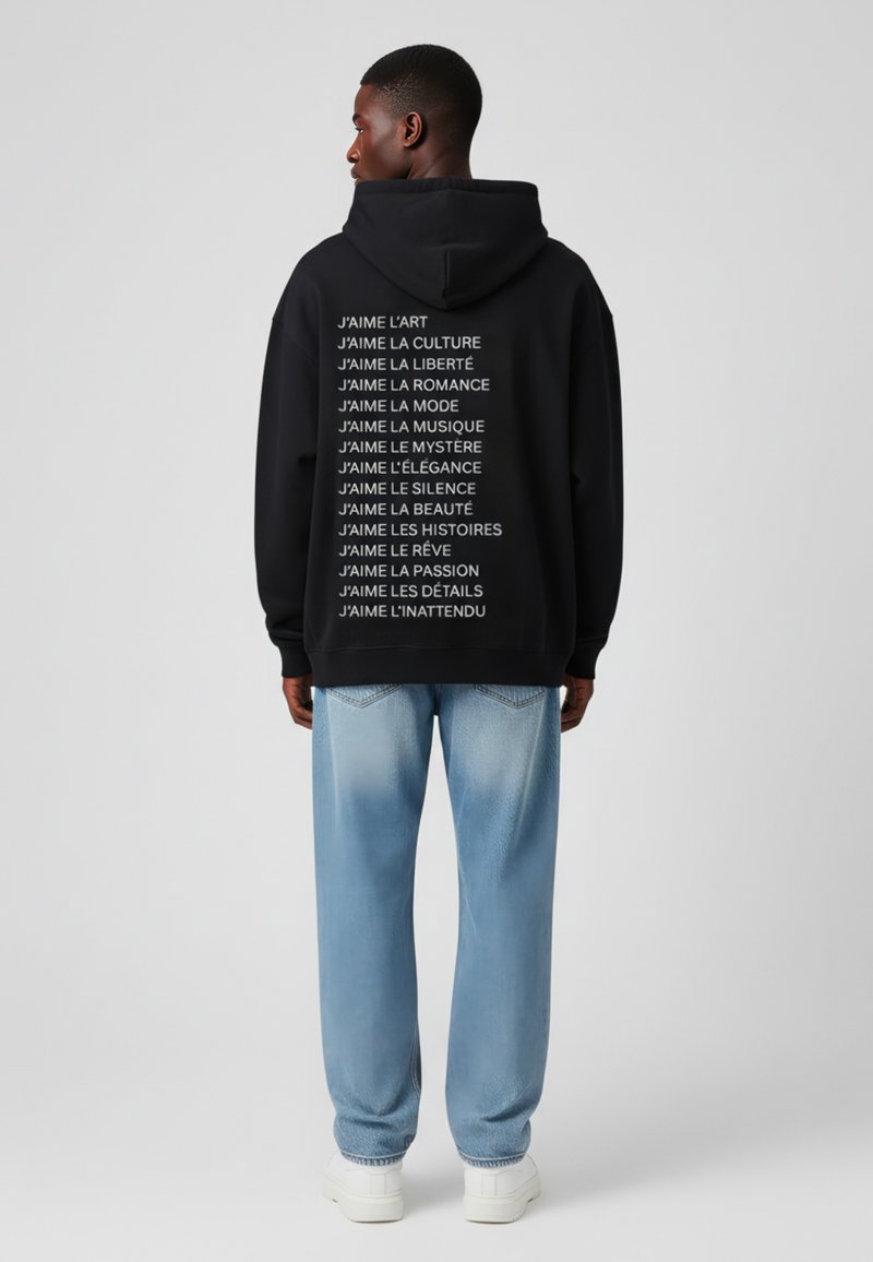 Sort hoodie i sort med hvid tekst på ryggen, der viser forskellige sætninger på fransk, parret med lyseblå straight-leg jeans og hvide sneakers.