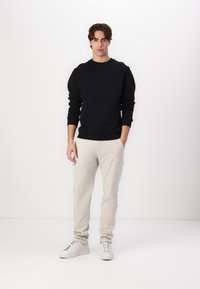 Zwarte sweatshirt, beige cargo broek, witte sneakers. Glad materiaal, ribgebreide manchetten, cargozakken op de broek, comfortabele pasvorm. Geen patronen of grafische elementen.