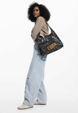 Čierna taška na rameno s grafickou potlačou obsahujúcou skice a slovo "DESIGNA" v žltej farbe. Mäkký materiál, priestranný dizajn a tkané doplnky.