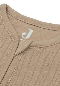 Beige katoenen vest met een textuur van ribvormig patroon, met een V-hals en contrasterende stiksels. Merklabel zichtbaar nabij de kraag.