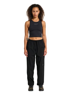 Young woman with curly hair stands facing forward, wearing a black sleeveless crop top and black cargo pants with hiking shoes.