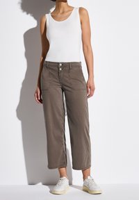 Bruna cropped byxor med framfickor och två-knapps stängning, ihop med en vit tanktop och vita sneakers. Slät tygkvalitet.