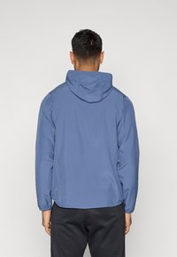 Μπλε ελαφρύ μπουφάν με κουκούλα, μαλακή υφή, ελαστικούς καρπούς και ίσια γραμμή. Διαθέτει ελάχιστες ραφές και κομψό σχέδιο.