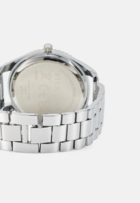 Montre en acier inoxydable argenté avec une finition brillante, dotée d'un bracelet à maillons et d'un boîtier rond avec couronne visible et fond gravé.