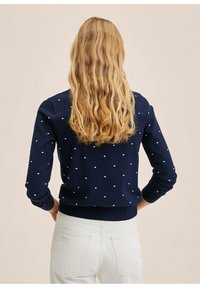 Pull en tricot bleu marine orné de pois blancs, avec des poignets et un ourlet côtelés. Le dos présente une coupe droite et un col rond simple.