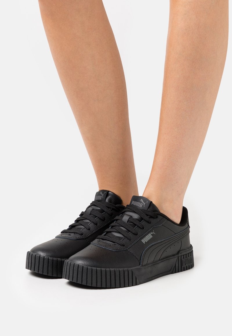 Baskets noires Puma avec semelles épaisses texturées portées pieds nus, montrant les détails latéraux et avant sur fond blanc.
