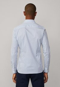 Biała koszula z długim rękawem z niebieskim geometrycznym wzorem. Posiada standardowy kołnierzyk i mankiety zapinane na guziki. Gładka tekstura.