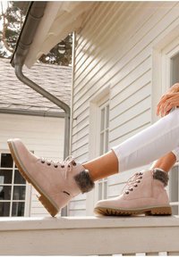 Botas de tobillo de color rosa claro, hechas de ante, con forro de piel sintética alrededor del puño, suela de goma gruesa y ojales de metal para los cordones.