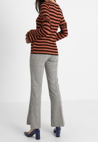 Svart och orange randig tröja med volangärmar, ihop med beige rutiga utsvängda byxor och blå klackskor.