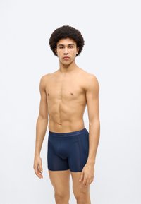 Σκούρα μπλε μποξεράκια από λείο, ελαστικό υλικό με εφαρμοστή σχεδίαση και ελαστική μέση που φέρει διακριτικό κείμενο με το σήμα.