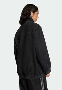 Črna jeans jakna s sproščenim krojem, z elastičnim robom in visokim ovratnikom. Pogled od zadaj prikazuje enostavno šivanje in brez vidnih naprav.