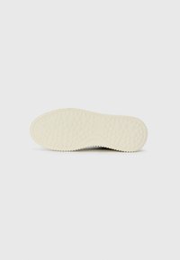 Sole of an off-white shoe with textured diamond and circular tread pattern on a plain white background.