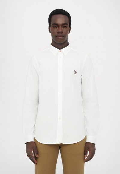 White long-sleeve shirt with a button-down collar and an embroidered horse logo on the chest, paired with tan pants. Smooth texture.
