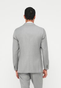 Completo a righe grigio chiaro con vestibilità sartoriale, giacca monopetto e pantaloni coordinati in tessuto strutturato con dettagli a bottoni.