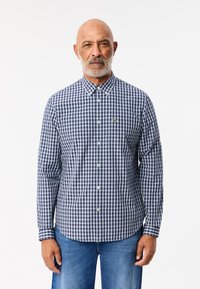 Camicia a maniche lunghe a quadri blu navy e bianca, con colletto abbassato, taschino sul petto e un piccolo logo verde sul lato sinistro.