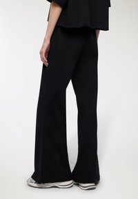 Pantaloni neri a gamba larga in tessuto liscio, con vita bassa e una sottile trama, abbinati a sneakers con dettagli argentati.