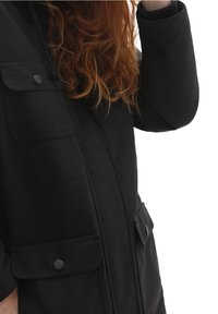 Zwarte jas met een gladde textuur, voorzien van twee voorste flapzakken, drukknoopsluitingen en een ontwerp met hoge kraag.