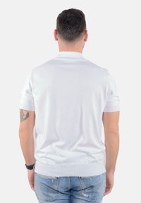 Polo shirt bianco a maniche corte con colletto e orlo a coste, texture morbida e design aderente, abbinato a jeans in denim azzurro chiaro.