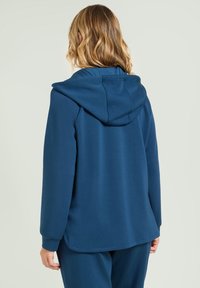 Felpa blu navy con vestibilità relaxed, tessuto morbido e cappuccio regolabile con cordino. Presenta maniche lunghe e orlo curvo.