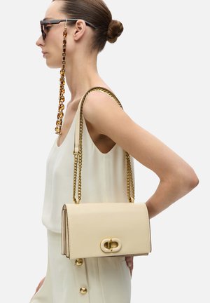 Beige leren handtas met een schakelriem, rechthoekige vorm, gladde afwerking, met een kenmerkende ovale sluiting en goudkleurige hardware.