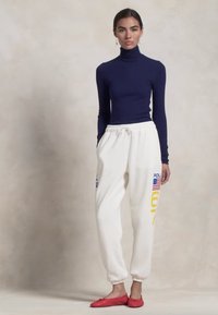 Ναυτικό πουλόβερ, λευκά παντελόνια φόρμας με μπλε και κίτρινες γραφικές παραστάσεις, ελαστική μέση, και κόκκινα flats. Λείος υφιστάμενος σε όλη την επιφάνεια.