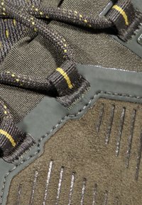 Szare zamszowe i tekstylne sneakersy z żółtymi szwami, teksturowanymi bocznymi akcentami i sznurówkami. Posiadają gumowe elementy i rowkowane wzory.