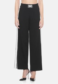 Pantaloni neri a gamba larga con una vita a coste che presenta un logo bianco. Strisce laterali con dettaglio testuale. Il materiale sembra liscio e leggero.