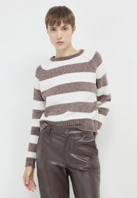 Gestreifter Pullover mit braun-weißen horizontalen Streifen, strukturierter Ripptextur und rundem Ausschnitt, kombiniert mit hochtaillierten braunen Lederhosen.