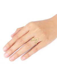 Gul zigzag-formet ring vist på en hånd med lys hud, der har en glat overflade og et åbent design.