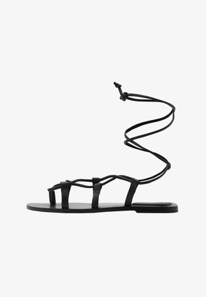 Black leather sandal featuring a flat sole, multiple straps, and an ankle tie that spirals upwards. Minimalist design with a smooth texture.