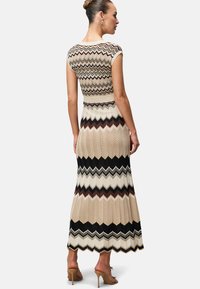 Maxi dress with a fitted cap-sleeve top and flared skirt. Features zigzag knit pattern in beige, black, and brown with a textured finish.