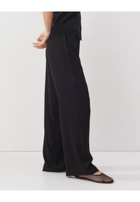 Czarne, szerokie spodnie z miękkiego materiału. Posiadają wysoki stan, subtelne fałdy i gładką teksturę. W zestawieniu z czarnymi płaskimi butami z siateczki.