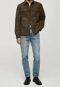 Brązowa koszula flanelowa z dwoma kieszeniami na piersi, w połączeniu z jasnoniebieskimi d�żinsami i czarnymi butami na sznurówki. Casualowy, luźny krój.