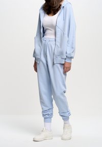 Blue hoodie and matching joggers in soft fabric, featuring a zip closure and elastic waistband. Complemented with white sneakers.