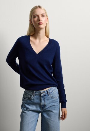 Marineblauwe v-hals trui van zacht materiaal, gecombineerd met lichtblauwe jeans in een klassieke pasvorm met subtiele zakdetails.