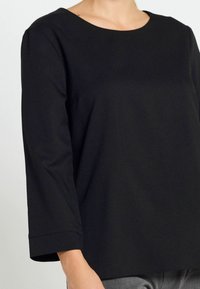 Top lungo nero a maniche lunghe con scollatura rotonda. Tessuto morbido e testurizzato con una vestibilità comoda e cuciture coperte. Design semplice, senza motivi o accenti.