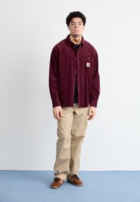 Bordeaux fløjl button-up skjorte med lommepatch, beige bukser og brune sneakers. Rent design med lange ærmer og afslappet pasform.