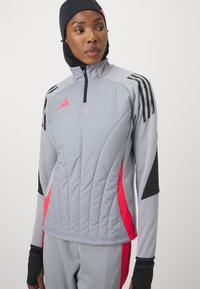 Chaqueta deportiva gris con acentos negros y detalles en rosa. Presenta un cuello alzado, cierre de media cremallera y un dise�ño de acolchado texturizado.